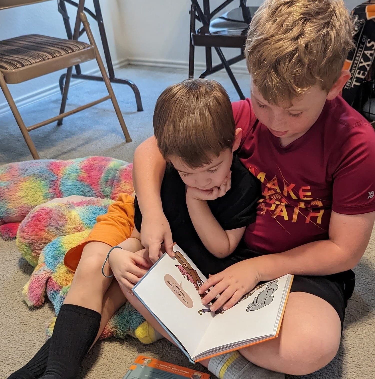 An older Crystal Challenges student reading a picture book aloud to a younger one, his arm around him.