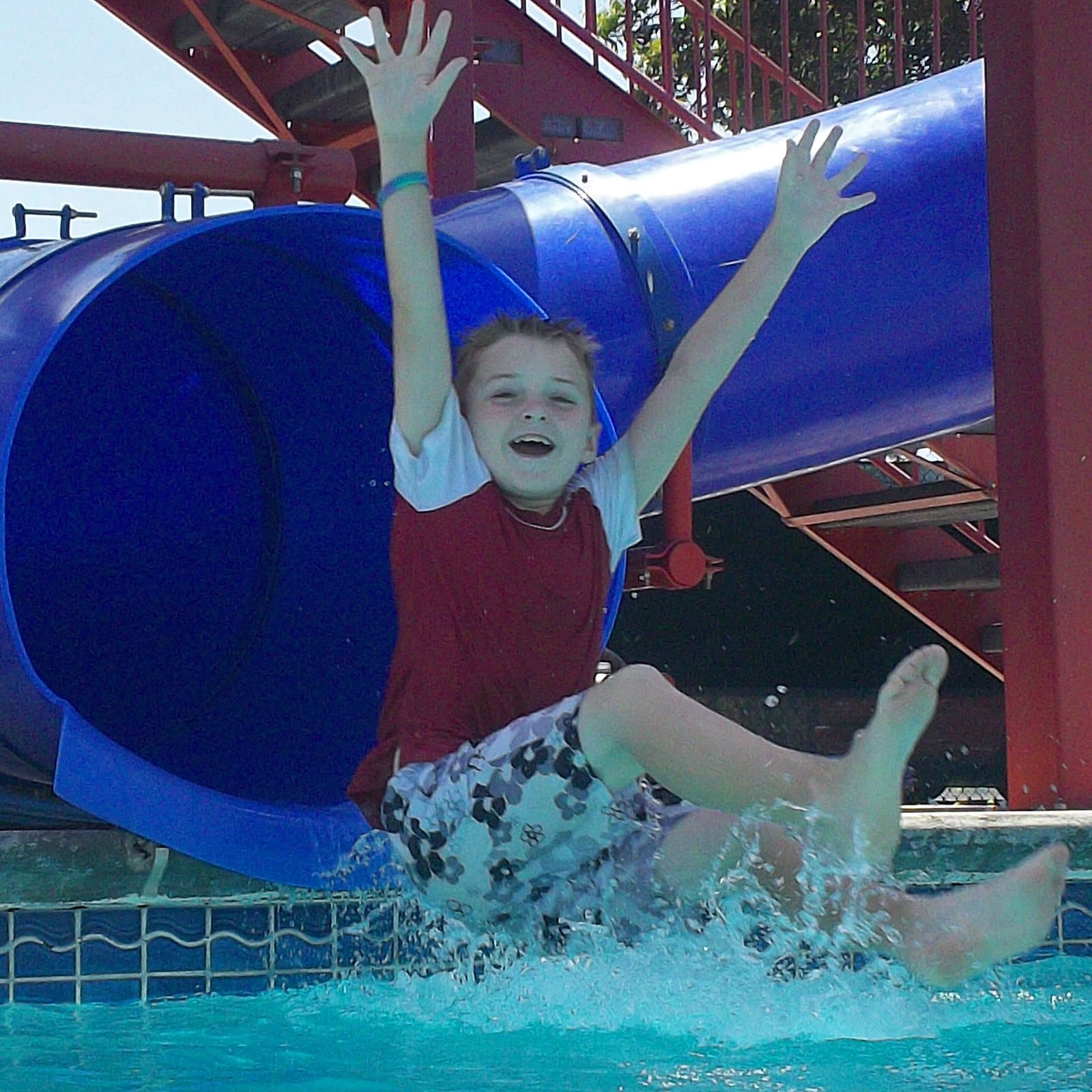 A Crystal Challenges camper flying off the end of the water slide into the pool, arms up and laughing.